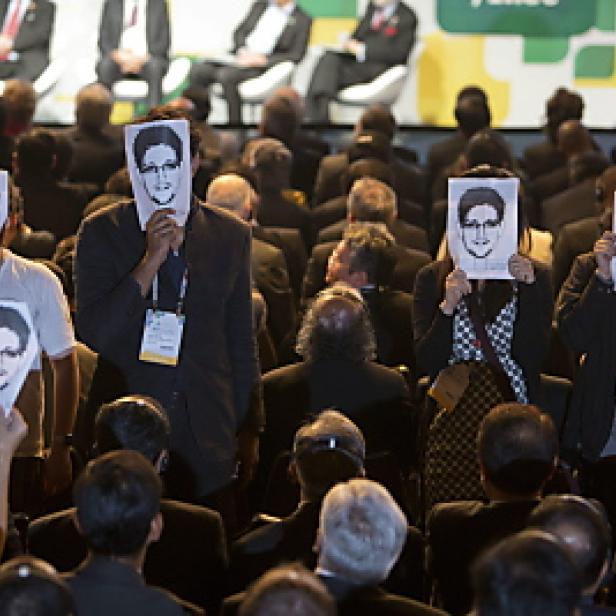 Menschen auf einer Konferenz halten Masken mit dem Gesicht von Edward Snowden hoch.