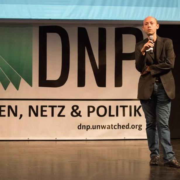 Ein Mann hält ein Mikrofon vor einem Banner mit der Aufschrift „DNP Daten, Netz & Politik“.