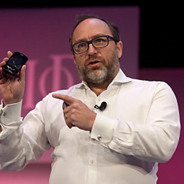 Ein Mann mit Brille präsentiert ein Mobiltelefon auf einer Bühne.