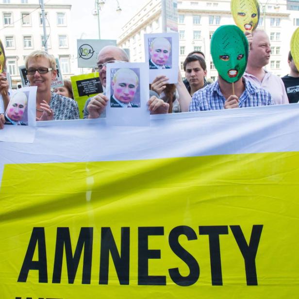 Menschen demonstrieren mit einem Banner von Amnesty International und Putin-Masken.