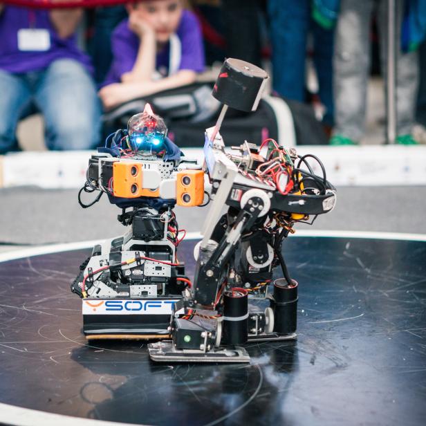 Zwei Roboter stehen auf einer runden Plattform vor Zuschauern.