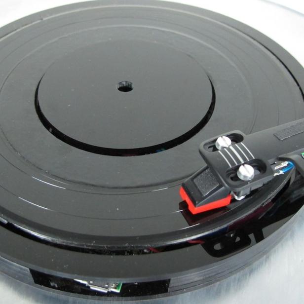 Ein Plattenspieler mit einer schwarzen Schallplatte und einem Tonarm.