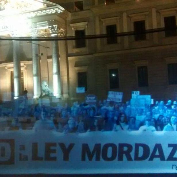 Eine Demonstration gegen das „Ley Mordaza“-Gesetz vor einem beleuchteten Gebäude.