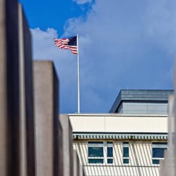 Die amerikanische Flagge weht über einem Gebäude, gesehen durch das Denkmal für die ermordeten Juden Europas.