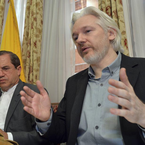 Julian Assange gestikuliert während einer Pressekonferenz neben einem Mann.