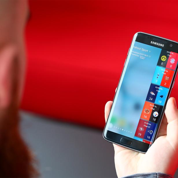 Eine Hand hält ein Samsung-Smartphone mit einer Sport-App, die Fußball- und Football-Ergebnisse anzeigt.