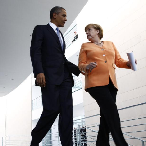 Barack Obama und Angela Merkel gehen in einem Gebäude die Treppe hinunter.