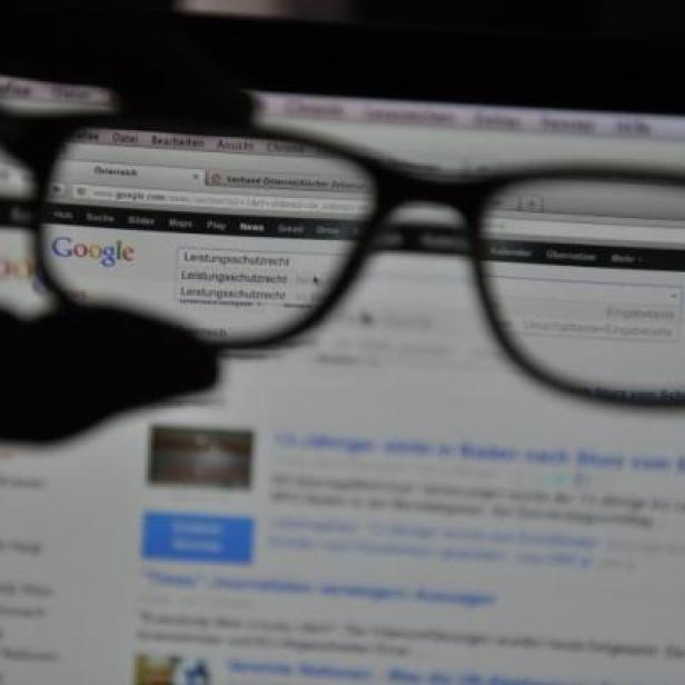 Eine Person hält eine Brille vor einen Laptop-Bildschirm mit der Google-Suchseite.