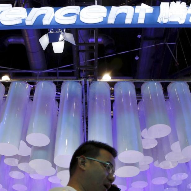 Ein Mann telefoniert unter dem beleuchteten Tencent-Logo und einer Installation aus Röhren.