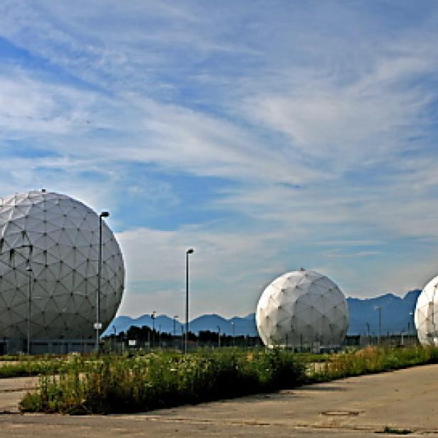 Drei große, kugelförmige Radome stehen auf einem Feld vor einer Bergkette.