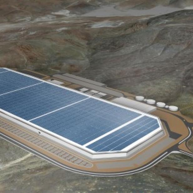 Luftaufnahme einer großen Solaranlage in einer Wüstenlandschaft mit Windkraftanlagen im Hintergrund.