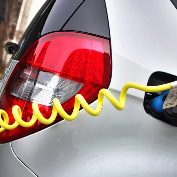 Ein Elektroauto wird an einer Ladestation mit einem gelben Kabel aufgeladen.