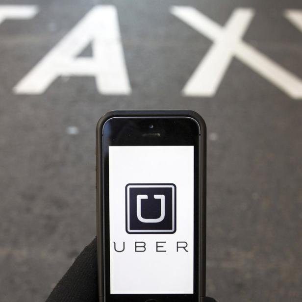 Ein Smartphone zeigt das Uber-Logo vor dem Schriftzug „Taxi“ auf der Straße.