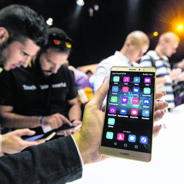 Eine Person hält ein goldenes Huawei-Smartphone in der Hand, während andere Personen im Hintergrund stehen.