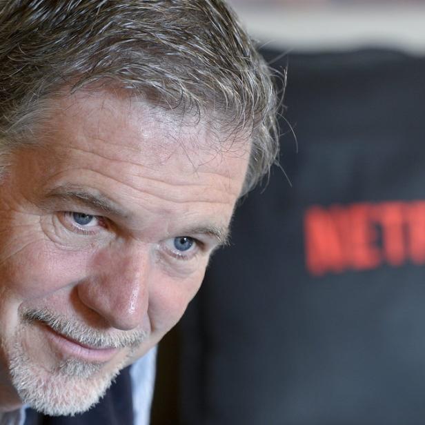 Ein Mann mit grauen Haaren lächelt vor einem Kissen mit dem Netflix-Logo.