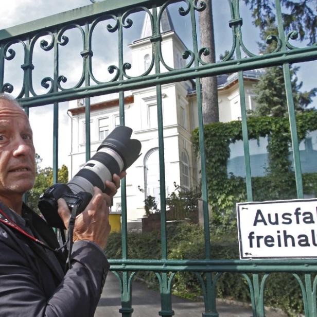 Ein Fotograf steht vor einem Tor mit dem Schild „Ausfahrt freihalten!“ und fotografiert ein Haus.