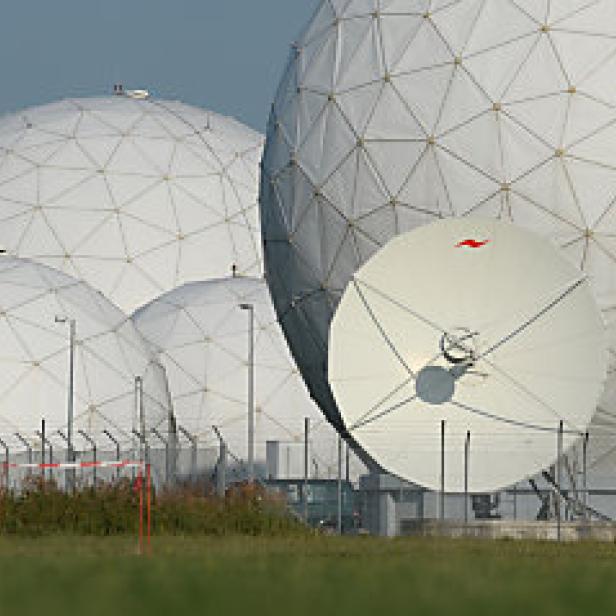 Mehrere weiße Radarkuppeln und eine Satellitenschüssel auf einem Feld.