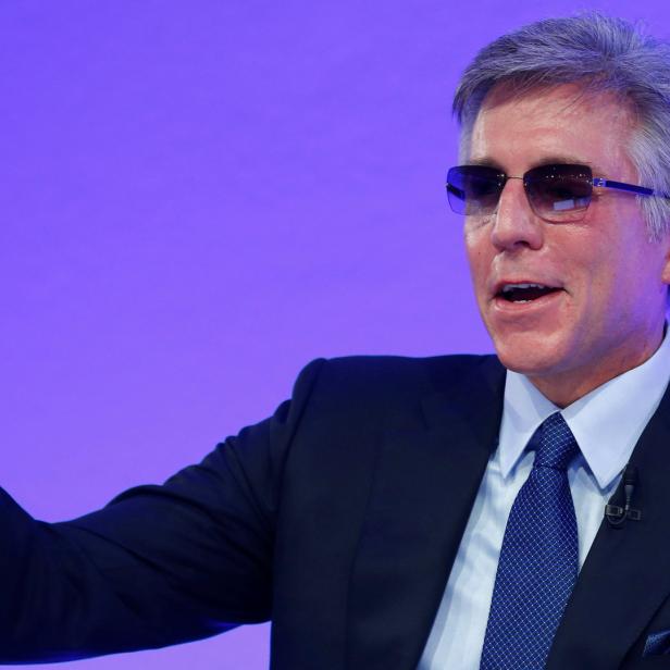 Ein Mann mit Anzug und Sonnenbrille hebt die Hand.
