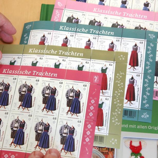 Eine Hand hält Blätter mit österreichischen Briefmarken, die klassische Trachten zeigen.