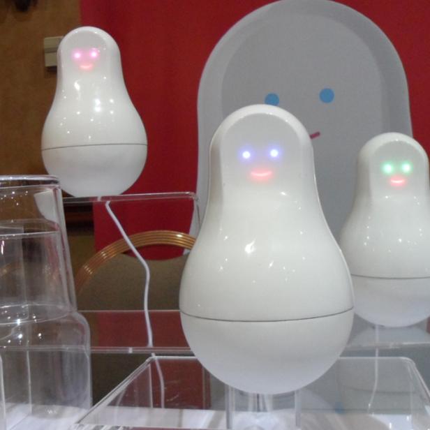 Drei weiße, birnenförmige Roboter mit leuchtenden Augen stehen auf einem Tisch.