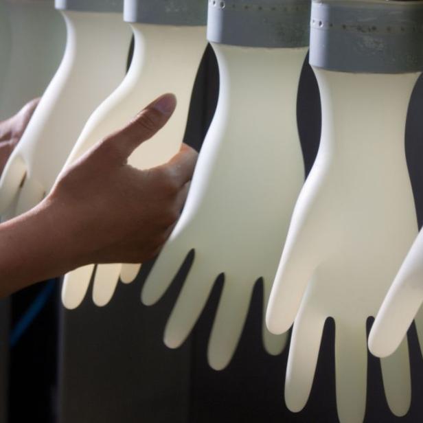 Eine Person im Laborkittel berührt eine Reihe von Gummihandschuhen.