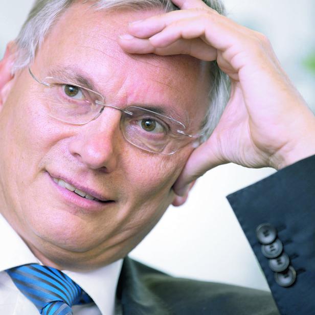 Ein Mann mit Brille und Anzug lächelt und stützt seinen Kopf mit der Hand.