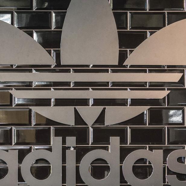 Das Adidas-Logo ist auf einer glänzenden, schwarzen Backsteinmauer angebracht.