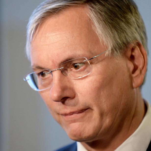 Ein Mann mit Brille und Anzug blickt leicht nach unten.
