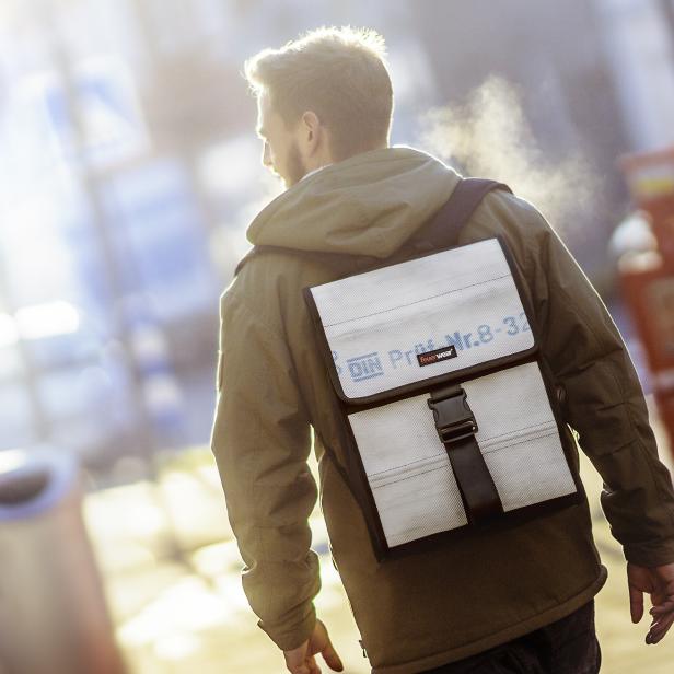 Ein Mann mit Jacke und Rucksack geht eine Straße entlang.