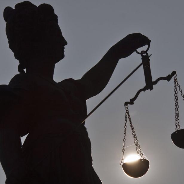 Die Silhouette der Justitia mit einer Waage vor einem hellen Hintergrund.