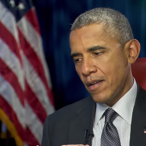 Barack Obama sitzt vor einer amerikanischen Flagge.
