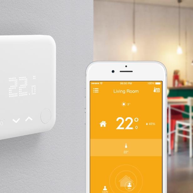 Ein Tado-Thermostat an der Wand und ein Smartphone mit der Tado-App, die 22 Grad anzeigt.