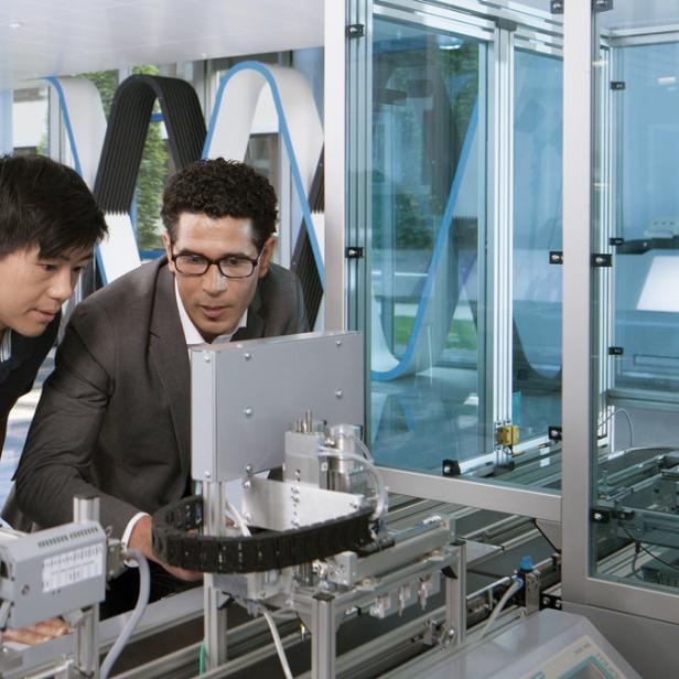 Zwei Männer arbeiten an einer industriellen Fertigungsanlage mit einem Roboterarm.