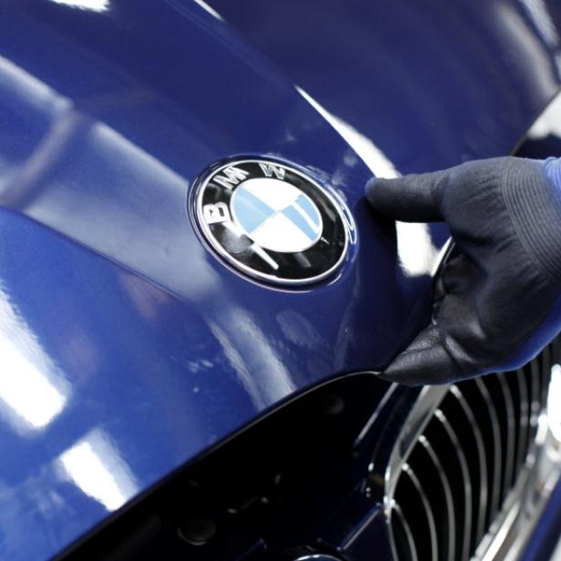 Eine Hand mit Handschuh berührt die Motorhaube eines blauen BMW.