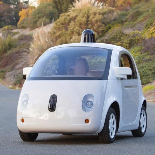 Ein weißes, selbstfahrendes Auto von Google auf einer asphaltierten Straße.