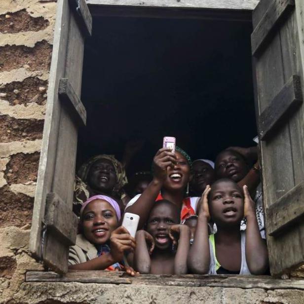 Eine Gruppe von Menschen, darunter Kinder, schaut aus einem Fenster und hält Mobiltelefone hoch.