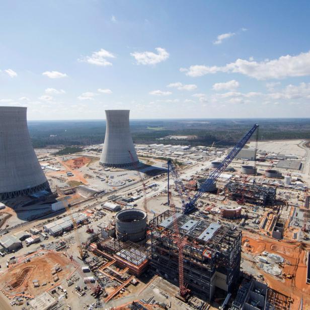 Luftaufnahme einer Baustelle mit zwei großen Kühltürmen im Hintergrund.