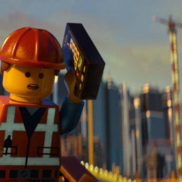 Eine Lego-Figur in Bauarbeiterkleidung hält ein Gerät vor einer Stadtkulisse.