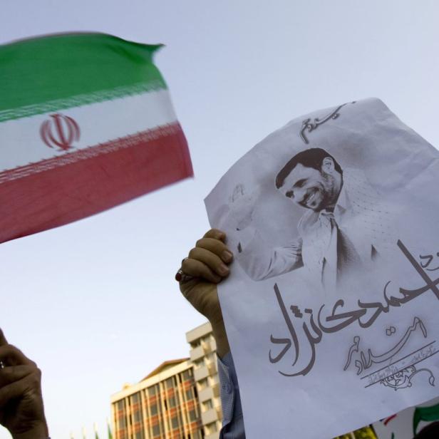 Eine Person hält eine iranische Flagge und ein Porträt von Mahmud Ahmadinedschad.