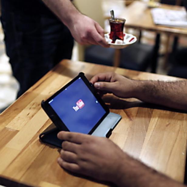 Ein Mann schaut auf einem Tablet in einem Café YouTube, während ihm Tee serviert wird.