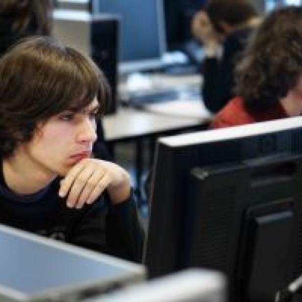 Ein junger Mann sitzt vor einem Computer und schaut konzentriert auf den Bildschirm.