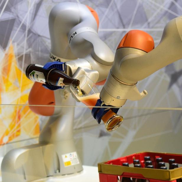 Ein Roboterarm der Marke KUKA zapft ein Bier in ein Glas.