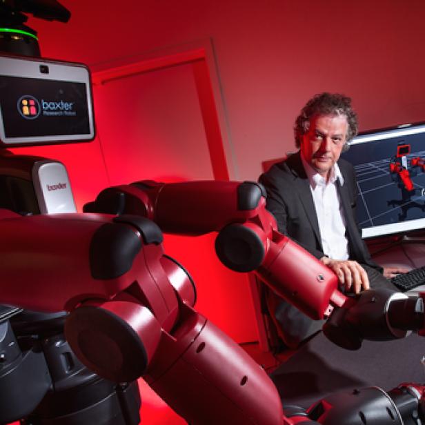 Ein Baxter-Roboter hantiert mit einer Dose, während zwei Männer daneben an einem Computer sitzen.