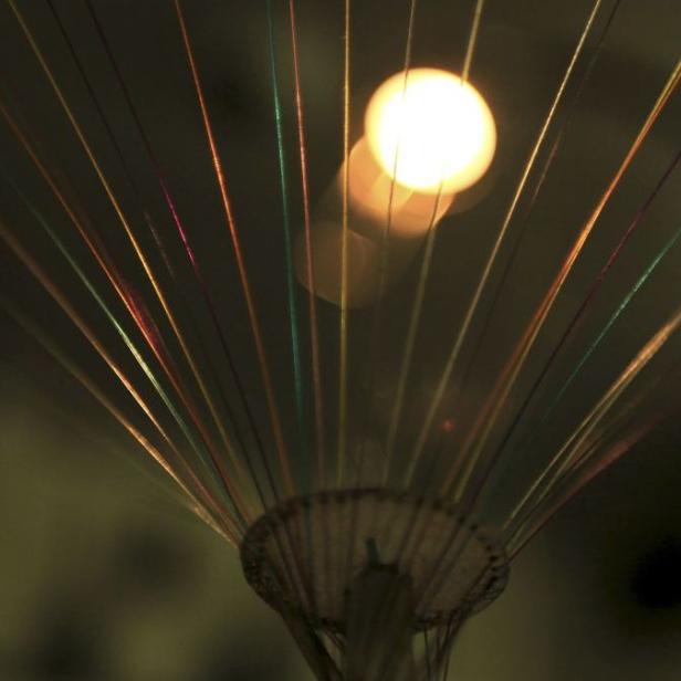 Mehrfarbige Fasern leuchten vor einem unscharfen Lichtpunkt.