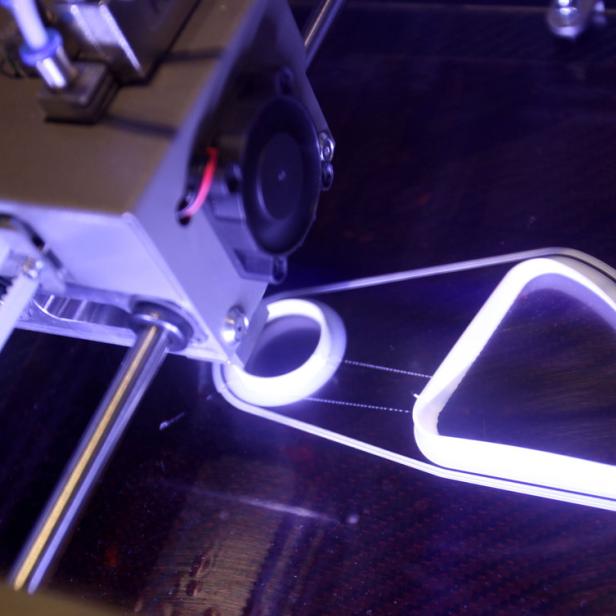 Ein 3D-Drucker druckt ein Objekt mit einer dreieckigen und einer runden Form.