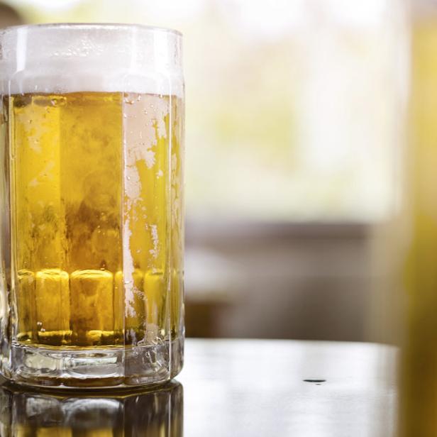 Ein großes Glas Bier mit Schaum steht auf einem Tisch.