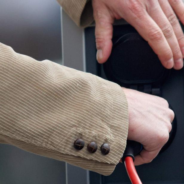 Eine Person schließt ein rotes Ladekabel an eine Ladestation für Elektroautos an.