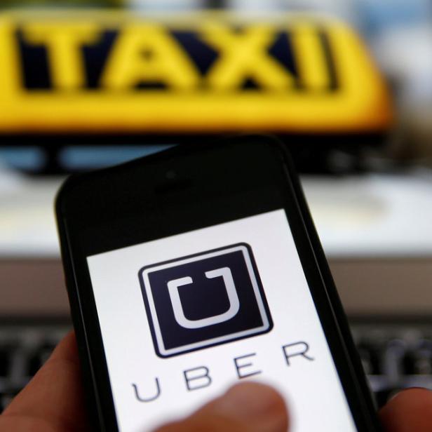 Ein Smartphone zeigt das Uber-Logo vor dem Hintergrund eines Taxi-Schilds.