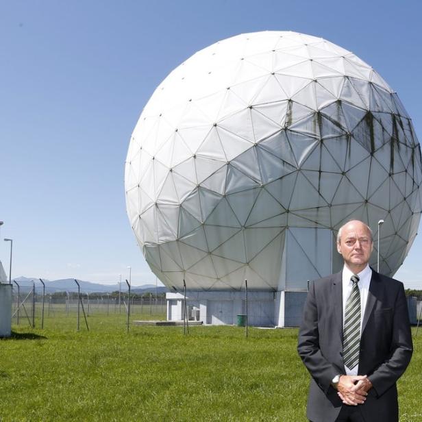 Ein Mann in Anzug steht vor einer Radaranlage mit mehreren geodätischen Kuppeln.