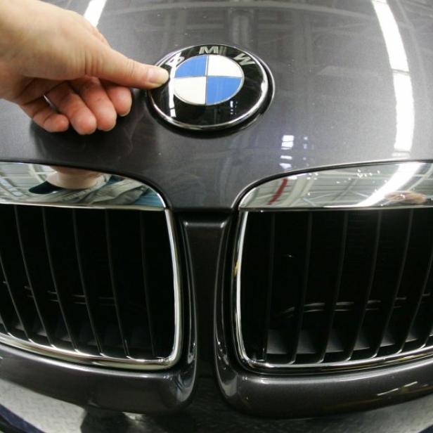 Eine Hand berührt das BMW-Logo auf der Motorhaube eines Autos.